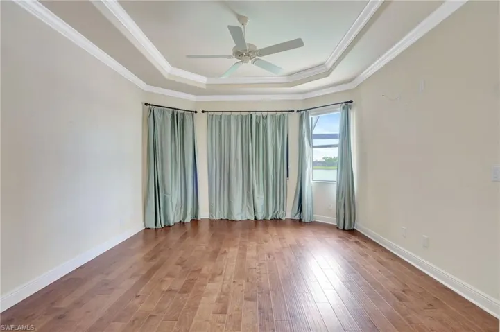 Empty room featuring ceiling fan, a raised ceiling, crown molding, and wood-type flooring