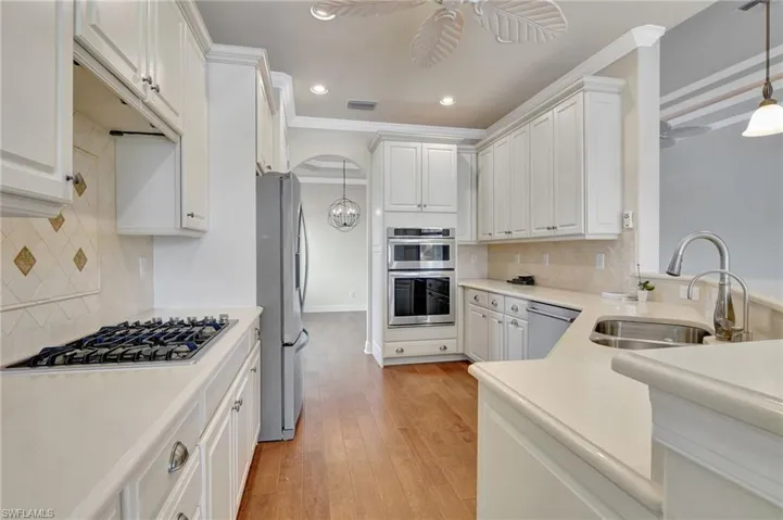 Kitchen with appliances with stainless steel finishes, light hardwood / wood-style flooring, ceiling fan, and tasteful backsplash