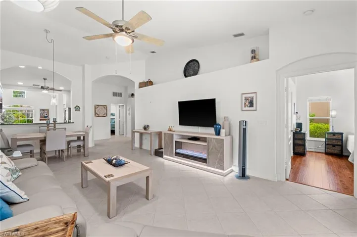 Spacious living area featuring neutral tile flooring, a vaulted ceiling with a ceiling fan, and arched doorways