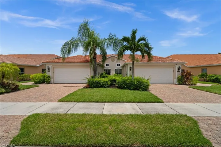 Mediterranean-style residence featuring a terracotta tile roof, paver driveway, and mature palm trees
