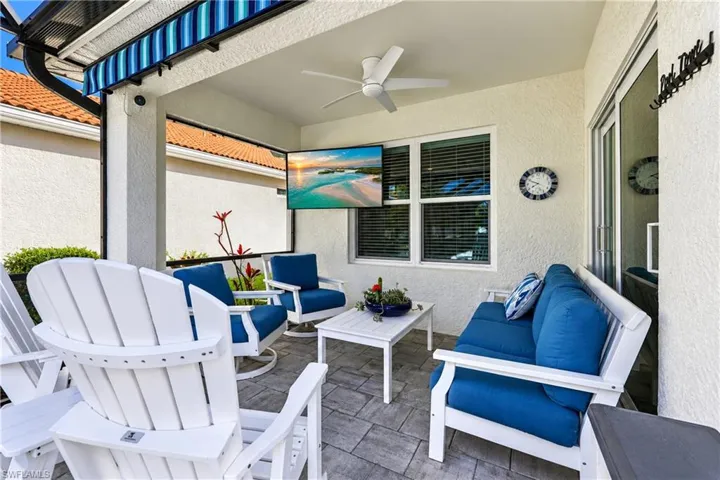 Covered patio featuring a ceiling fan, wall-mounted television, sliding glass door, and a striped awning