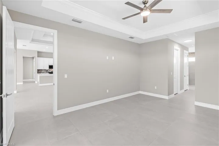 Unfurnished room featuring a raised ceiling, light tile patterned floors, crown molding, a ceiling fan, and recessed lighting