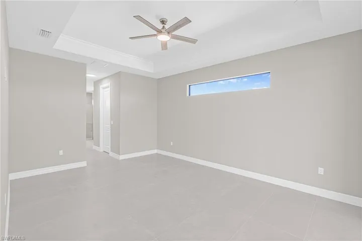 Unfurnished room featuring a raised ceiling, light tile patterned flooring, and a ceiling fan