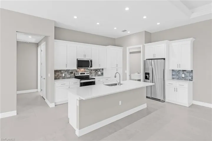 Kitchen with stainless steel appliances, white cabinetry, decorative backsplash, recessed lighting, and an island with sink