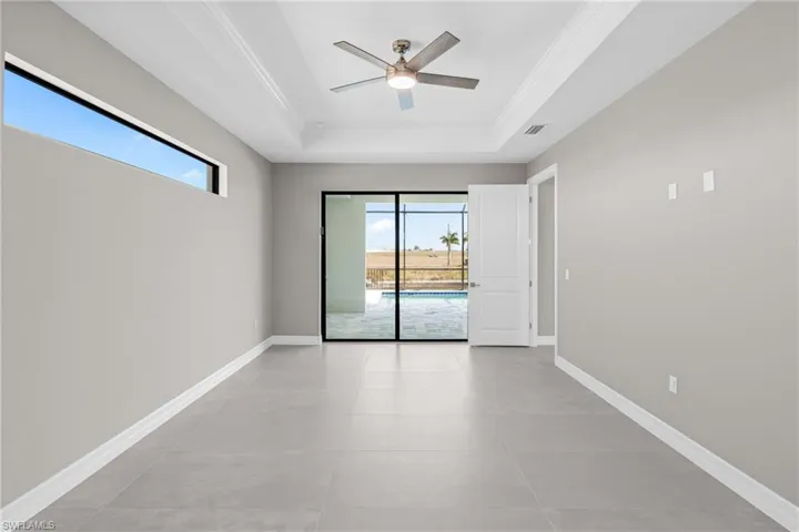 Spare room with healthy amount of natural light, a tray ceiling, a ceiling fan, crown molding, and light tile patterned floors