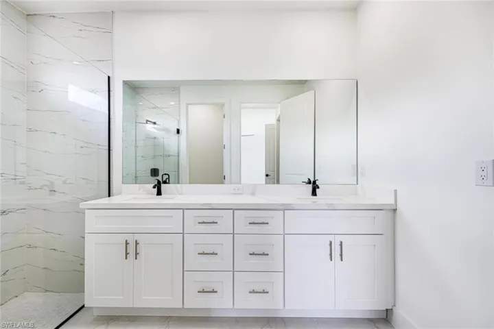 Full bath with double vanity, a marble finish shower, and light marble finish flooring