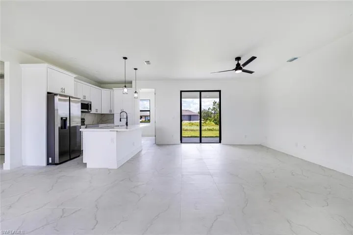 Kitchen with open floor plan, stainless steel appliances, white cabinets, an island with sink, and pendant lighting