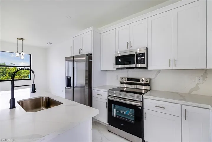 Kitchen with stainless steel appliances, white cabinets, and light stone countertops