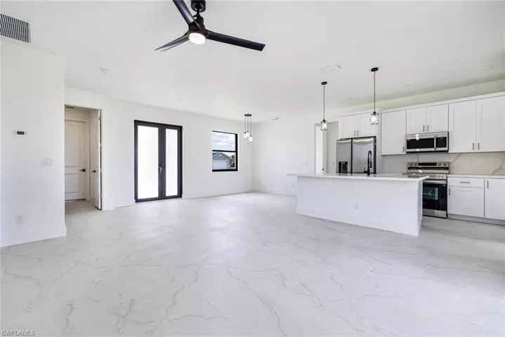 Kitchen featuring open floor plan, stainless steel appliances, white cabinetry, and a ceiling fan
