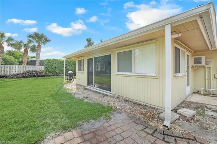 View of side of home featuring a lawn and an AC wall unit