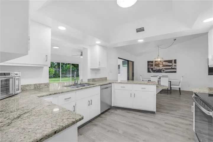 Kitchen with white cabinets, ceiling fan with notable chandelier, stainless steel appliances, light hardwood / wood-style floors, and kitchen peninsula