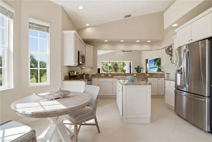 Kitchen with lofted ceiling, stainless steel appliances, light stone counters, white cabinets, and a kitchen island