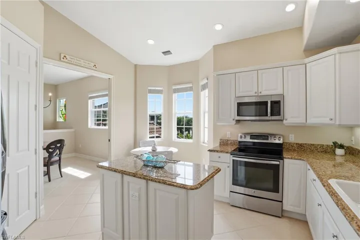 Kitchen with stainless steel appliances, a kitchen island, white cabinetry, light tile patterned flooring, and light stone counters