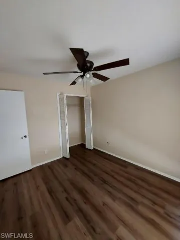 Unfurnished bedroom featuring dark wood-style flooring, a closet, and a ceiling fan
