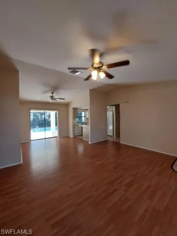 Unfurnished living room featuring dark wood finished floors, vaulted ceiling, and ceiling fan