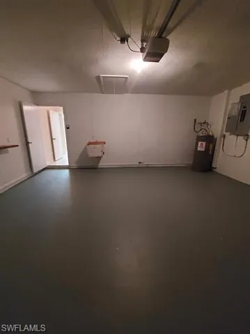 Garage with water heater, electric panel, and a garage door opener