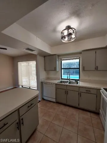 Kitchen featuring light countertops, light tile patterned floors, white appliances, a textured ceiling, and gray cabinetry
