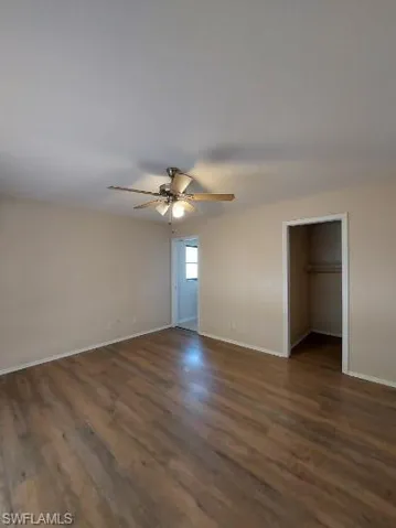 Unfurnished bedroom with a walk in closet, dark wood finished floors, and a ceiling fan