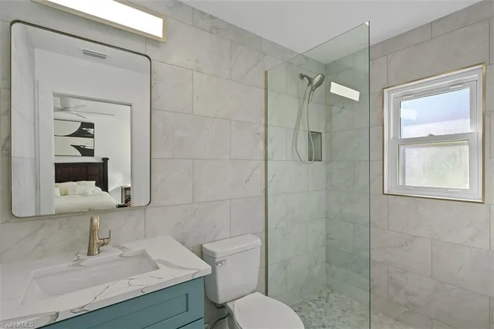 Full bathroom featuring tile walls, a walk in shower, vanity, and connected bathroom