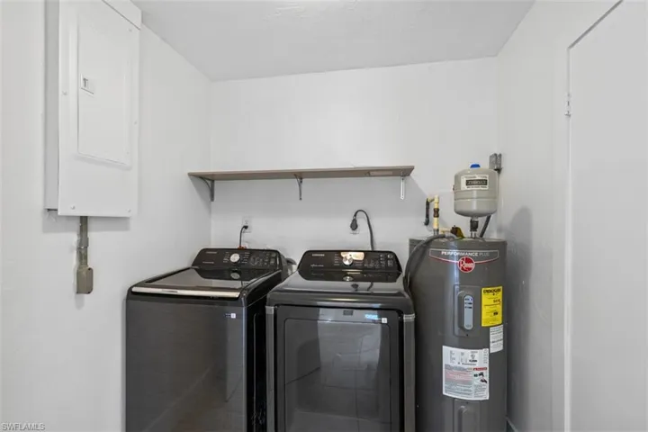 Laundry room with electric water heater, electric panel, and washer and clothes dryer