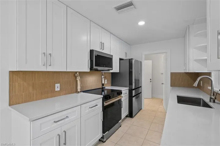 Kitchen with open shelves, white cabinetry, appliances with stainless steel finishes, light stone countertops, and light tile patterned floors