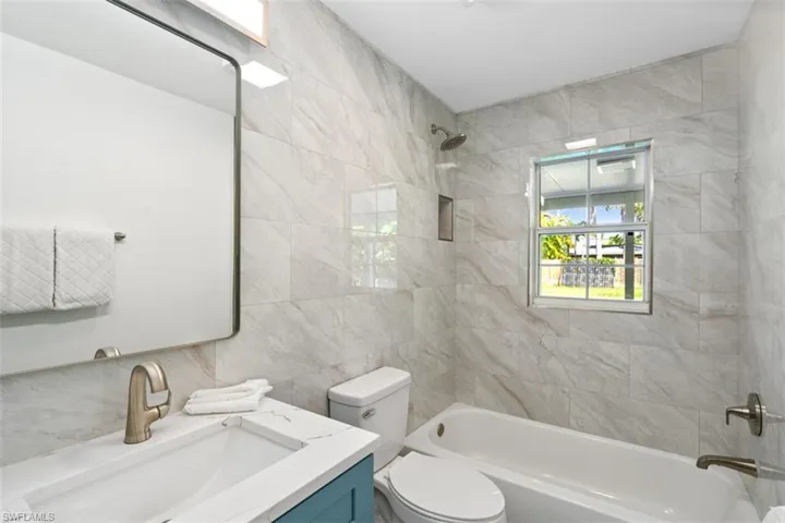 Bathroom with vanity, shower / tub combination, and tile walls