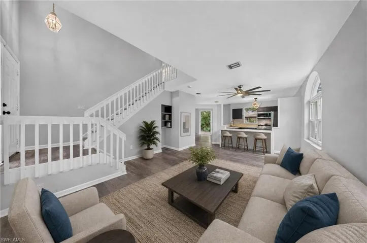 High ceilings, staircase with white banister, wood-finish flooring, built-in shelving, and arched window
