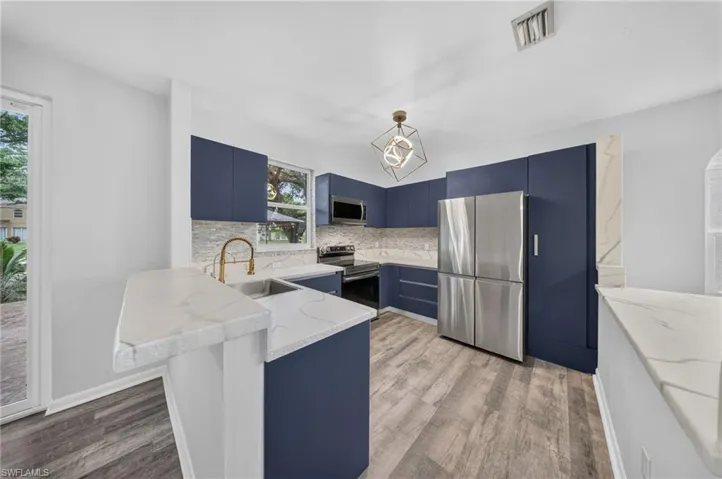 Contemporary kitchen featuring blue cabinetry, white countertops, stainless steel appliances, wood-finish flooring, and a unique geometric light fixture