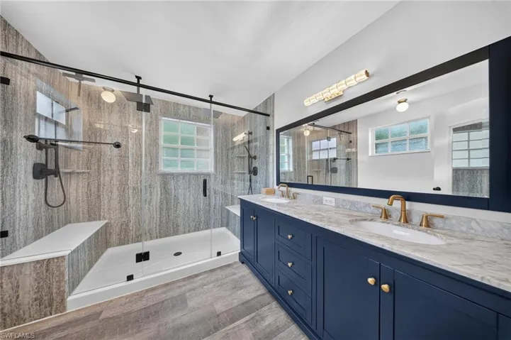 Dual vanity with blue cabinetry, gold-toned fixtures, and a large framed mirror