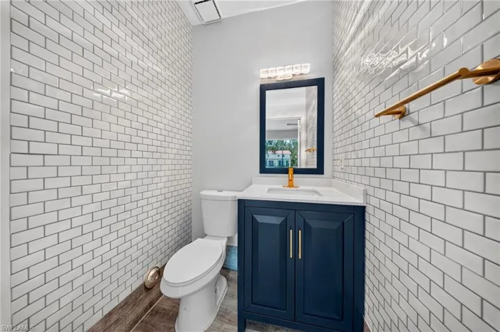Subway tile walls, wood-finish flooring, dark blue vanity with gold-tone hardware, white countertop, and gold-tone faucet