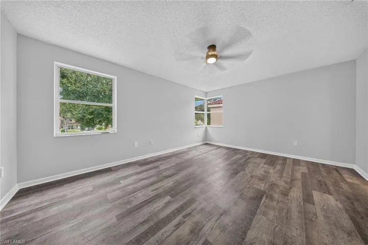 Spacious room featuring wood-finish flooring, light grey walls, and a ceiling fan