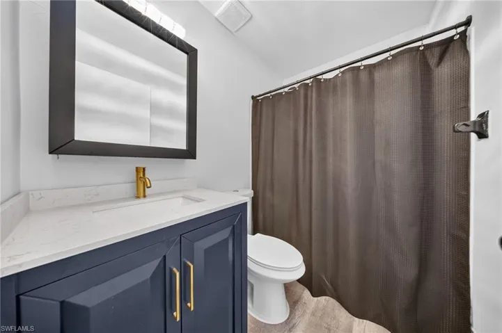 Vanity with a quartz-finish countertop and integrated sink, gold-tone faucet, and dark blue cabinetry with gold-tone hardware