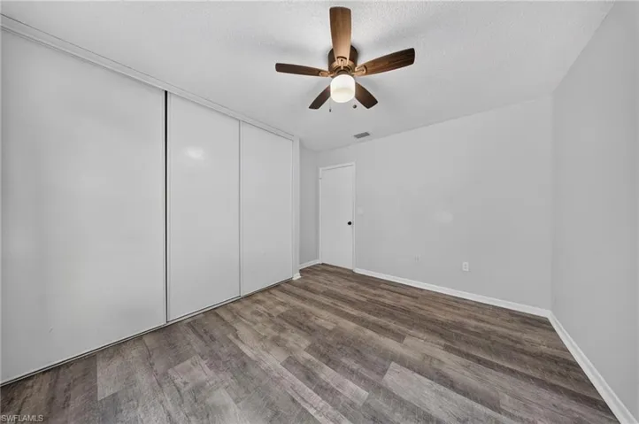 Wood-finish flooring, white walls, built-in closet with sliding doors, and a ceiling fan with integrated lighting