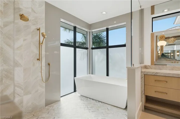 Contemporary bathroom featuring a freestanding soaking tub, a large walk-in shower with gold-tone fixtures, and a vanity with a stone countertop and integrated sink - Virtually Edited Image