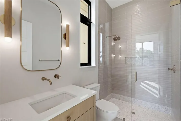 Modern bathroom featuring a walk-in shower with textured tile, a rain showerhead, a built-in shower niche, and a frameless glass enclosure