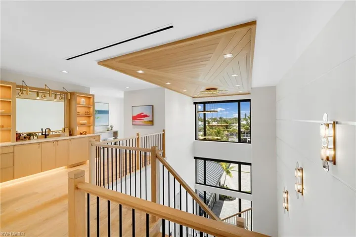 Multi-level interior featuring a wood-finish staircase with black metal balusters, a wood-paneled ceiling accent, and a built-in wet bar with wood cabinetry and under-cabinet lighting