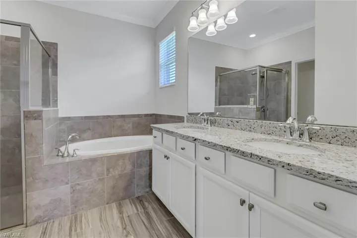 Primary Bathroom featuring a shower stall, double vanity, a bath, and ornamental molding