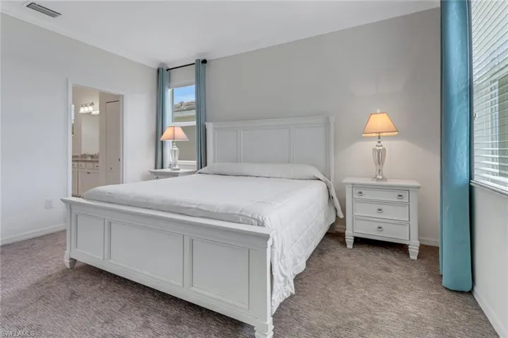 Primary Bedroom with carpet, multiple windows, ensuite bath, and crown molding
