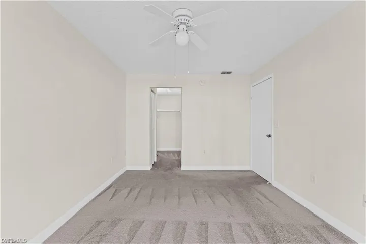 Unfurnished bedroom featuring a walk in closet, light carpet, ceiling fan, and a textured ceiling