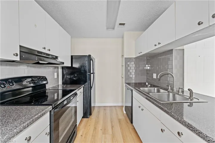 Kitchen featuring black appliances, white cabinetry, under cabinet range hood, decorative backsplash, and a textured ceiling