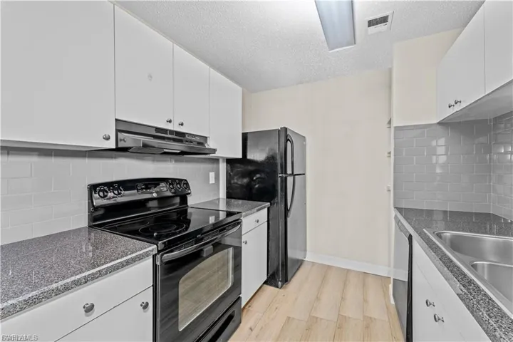 Kitchen featuring black electric range oven, white cabinets, decorative backsplash, and a textured ceiling