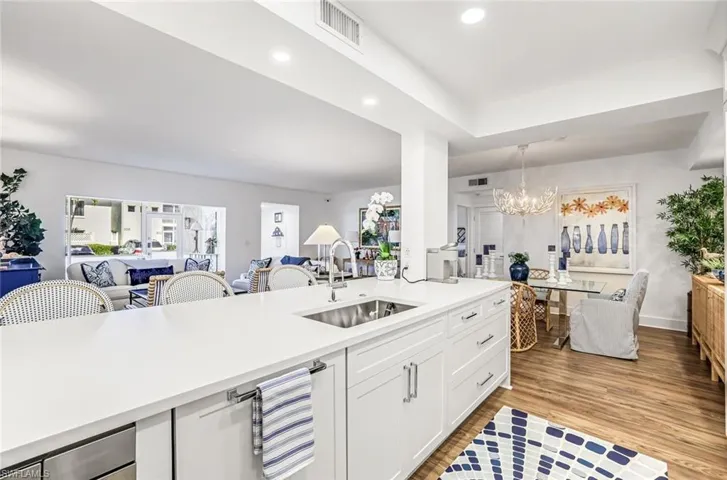Kitchen featuring open floor plan, white cabinets, light wood-style floors, suspended lighting, and light stone counters