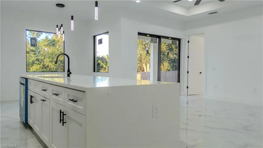 Kitchen with white cabinets, pendant lighting, light stone countertops, light marble finish floors, and an island with sink