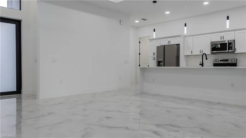Kitchen featuring white cabinets, appliances with stainless steel finishes, hanging light fixtures, light marble finish floors, and a breakfast bar