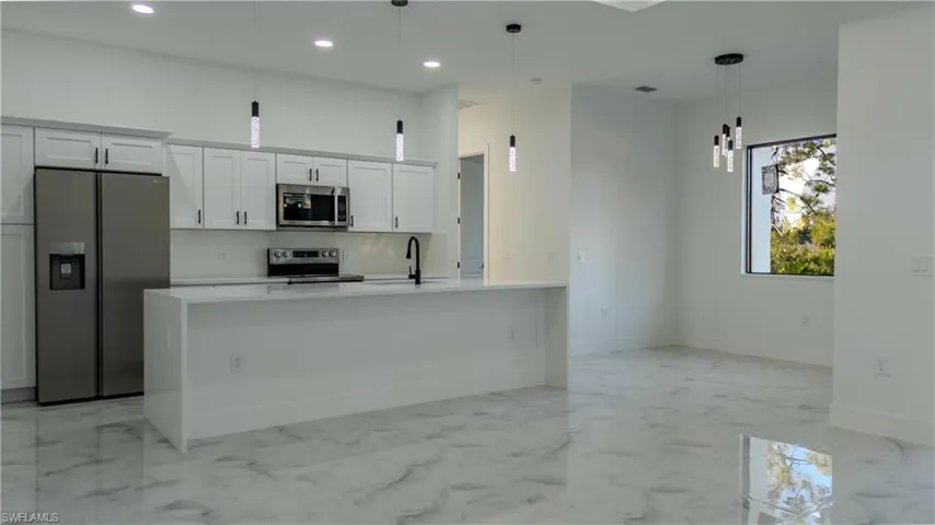 Kitchen featuring appliances with stainless steel finishes, white cabinetry, light stone countertops, pendant lighting, and light marble finish floors