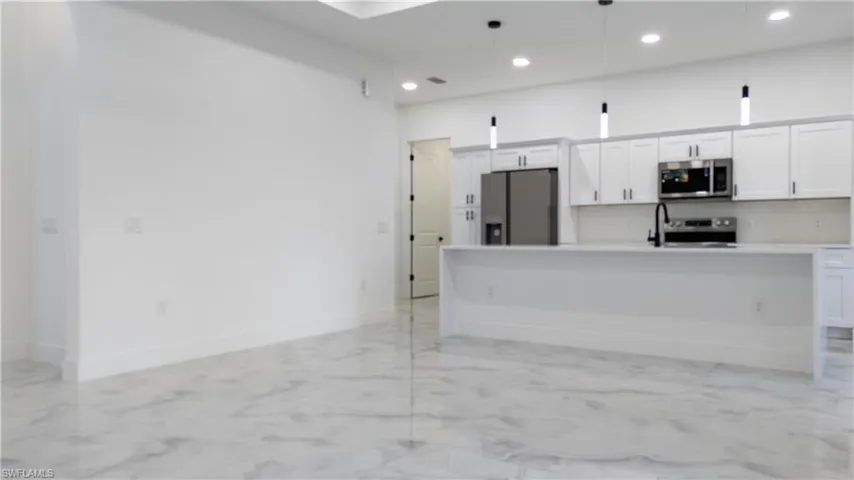 Kitchen featuring white cabinets, appliances with stainless steel finishes, a kitchen island with sink, light marble finish flooring, and hanging light fixtures