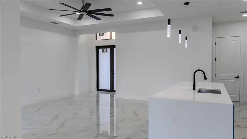 Kitchen with decorative light fixtures, light marble finish floors, light stone countertops, a raised ceiling, and recessed lighting