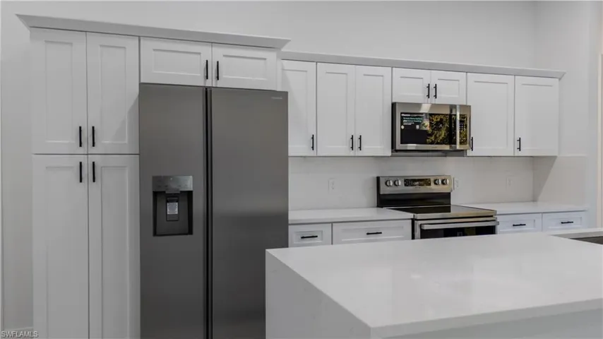 Kitchen with appliances with stainless steel finishes, white cabinets, light stone countertops, and decorative backsplash