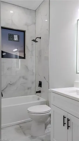 Bathroom with vanity, tub / shower combination, and light marble finish floors