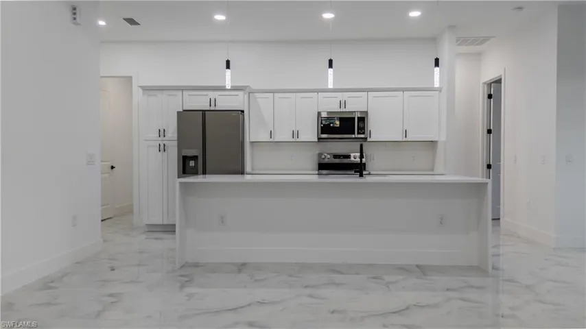 Kitchen with white cabinets, appliances with stainless steel finishes, recessed lighting, light marble finish floors, and pendant lighting